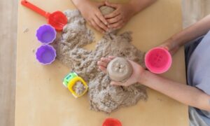 Kinetički pijesak u igri: dječje ruke oblikuju pijesak uz kalupe i alate.