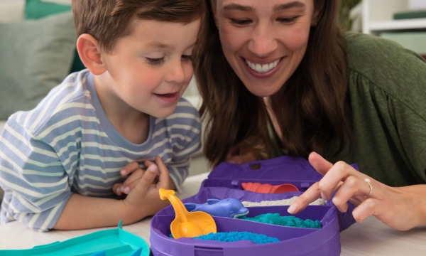 Mama i dijete oblikuju kinetički pijesak u posudi uz lopaticu i kalupe.